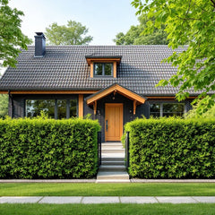 En vacker villa med svart fasad och trädetaljer, omgiven av en tät, grön thujahäck.